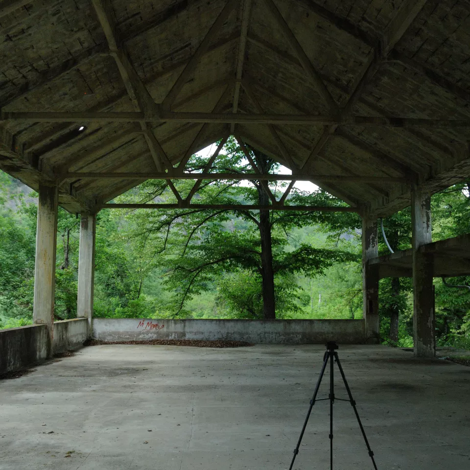A large concrete hangar on the upper floor, open to nature, with a tripod placed in the foreground.